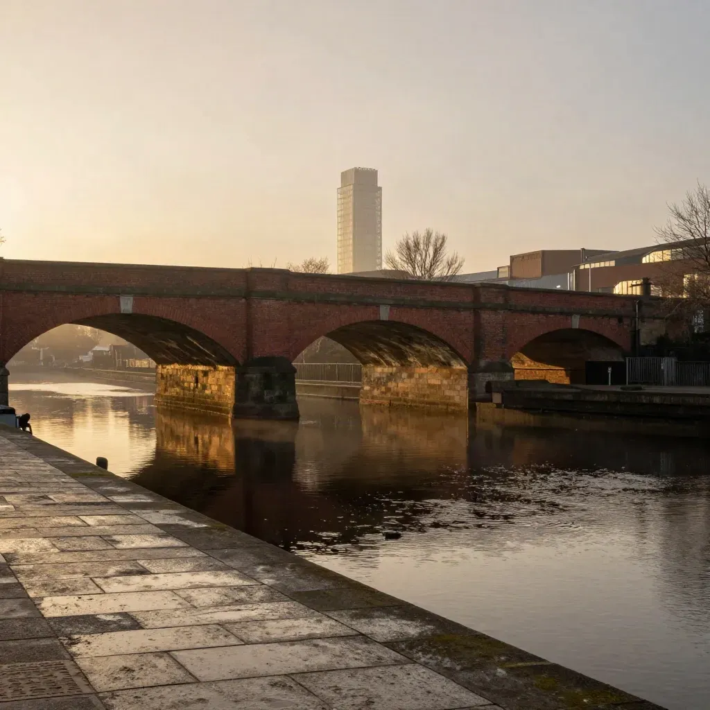 Birmingham canal basin at sunset with redbrick arches, calm water, and a distant tower